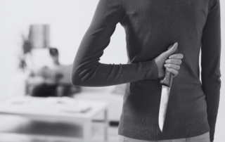 A woman in a dark dress hiding a kitchen knife behind her back.