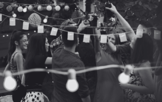 Guests dancing outdoors in the evening under strings of party lights.
