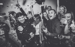 A crowd of party guests cheering with their arms in the air as confetti falls.