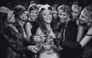 Guests in 1920s dresses and headbands toasting with champagne at a party.