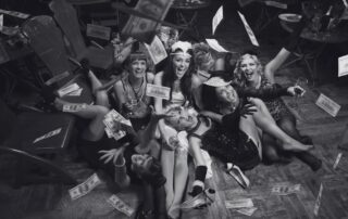 Costumed party guests sitting on the floor laughing, with notes and cash scattered around them.