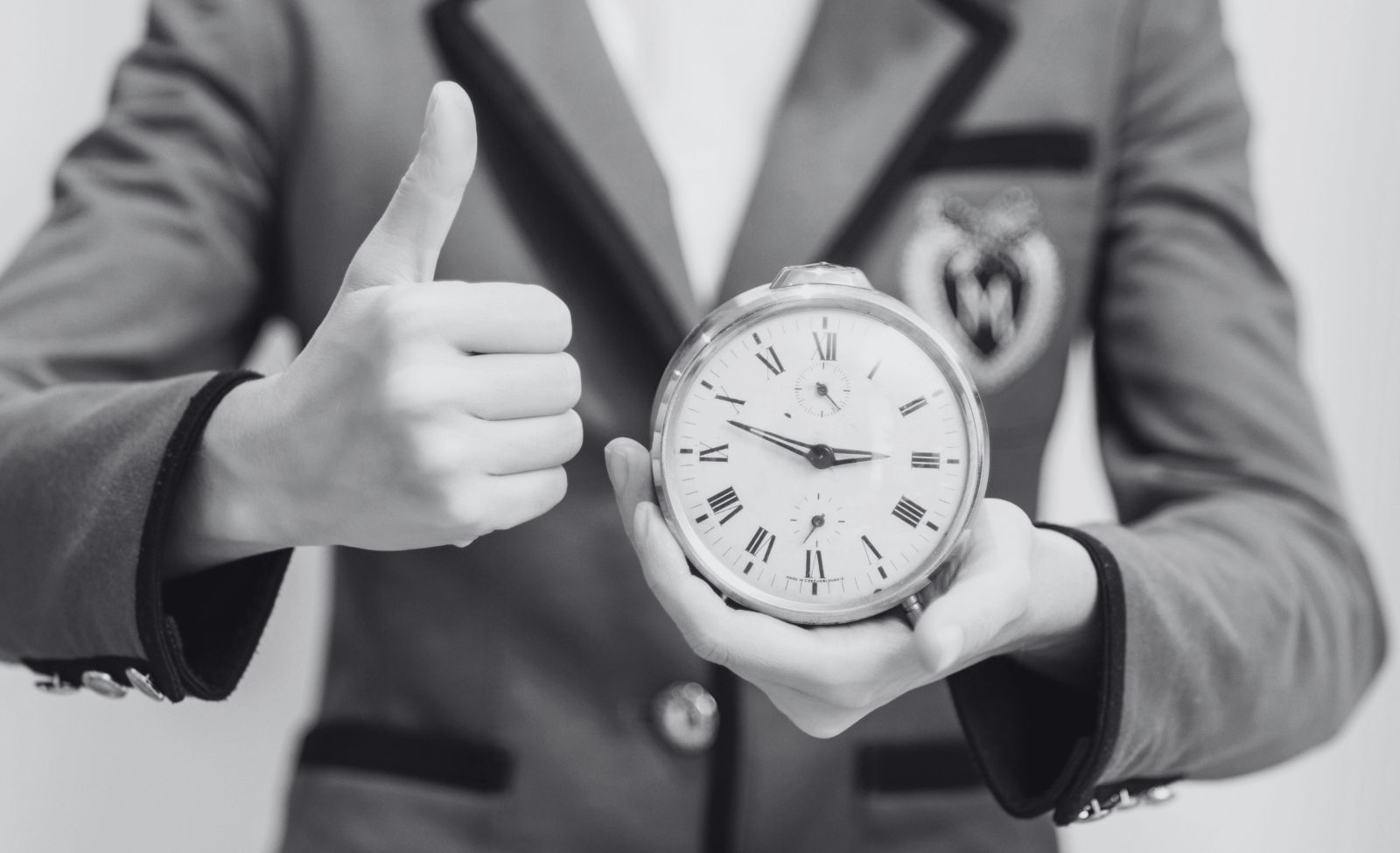 A man in a suit holding up a clock and giving a thumbs up.