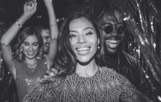 A group of friends dancing and laughing at a party in sequins and glitter.