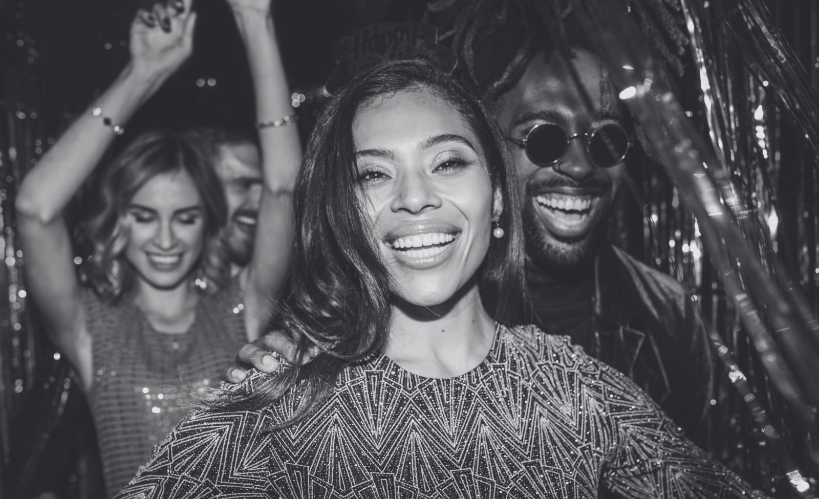 A group of friends dancing and laughing at a party in sequins and glitter.