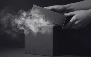 Hands lifting the lid of a box with smoke pouring out of it.