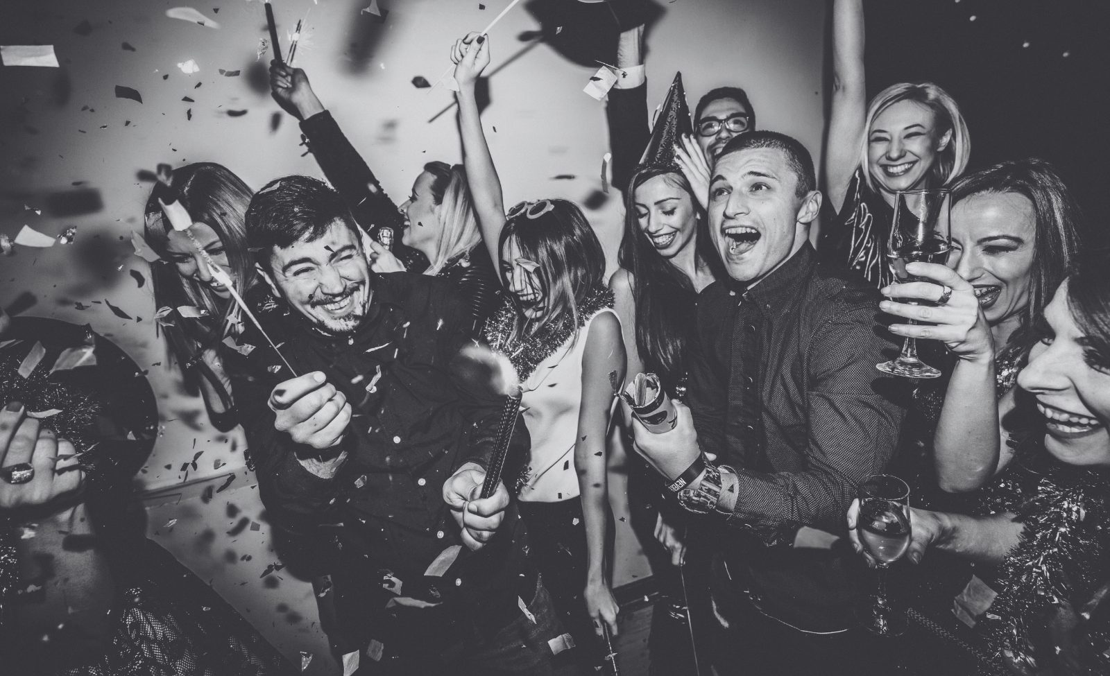 A crowd of party guests cheering with their arms in the air as confetti falls.