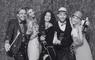 5 guests in party clothes posing together with champagne and party props.