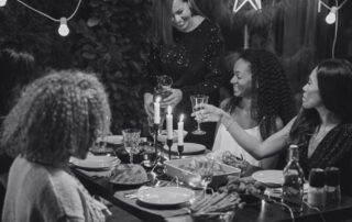 Guests laughing around a candlelit dinner table set with glasses and bottles.