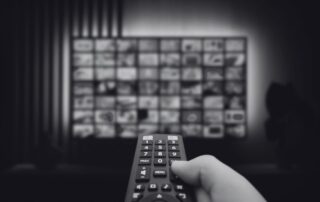 A hand holding a remote control in front of a wall of television screens.