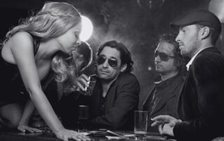 Party guests in sunglasses and evening clothes gathered at a bar.