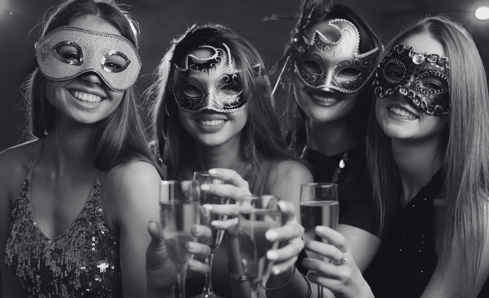 Women in masquerade masks raising champagne glasses together.