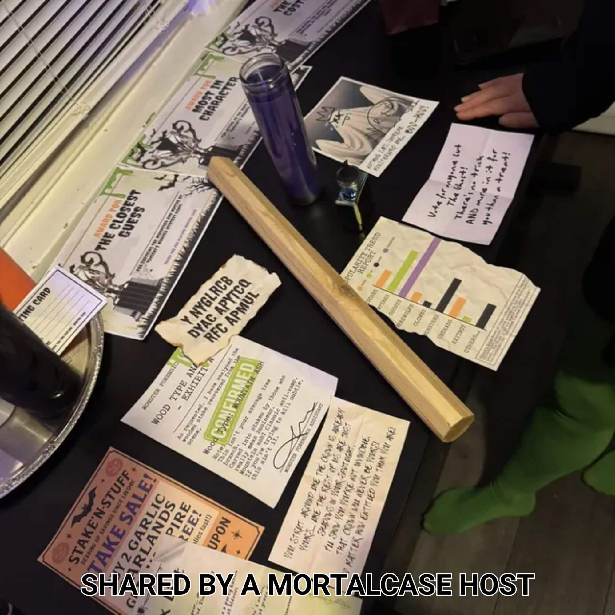 Murder Among Monsters clues, evidence cards and a wooden weapon prop arranged on a party table.